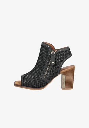 Sandale noire à talon ouverte à l'avant, texture tissée, fermeture éclair latérale, détails cloutés et talon à blocs en bois empilés avec étiquette métallique de marque.