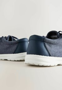 Marineblaue Stoff-Sneaker mit texturiertem Obermaterial, glatten Lederelementen, kontrastierender weißer Sohle und verstärkten Nähten. Für Komfort konzipiert.