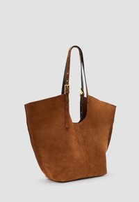 Borsa tote in suede marrone con un ampio apertura superiore, manici in pelle nera e dettagli in metallo dorato. Texture liscia e design minimalista.