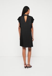 Čierne šaty s krátkymi volánovými rukávmi, detailom na chrbte v podobe slzičky a okrúhlym výstrihom ozdobeným cvočkami. Hladká textúra, dĺžka po kolená.