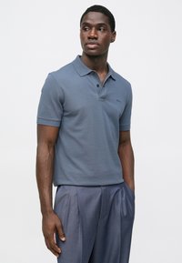 Férfi rövid ujjú galléros póló sötétkék anyagból, klasszikus gallérral, háromgombos patenttal és finom logóval a mellrészen.