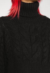 Czarny sweter z golfem wykonany z dzianiny, z fakturą w warkocze i prążkowanym kołnierzem. Materiał wydaje się gruby i puszysty, co zwiększa ciepło.