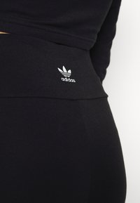 Gros plan sur des vêtements de sport noirs Adidas montrant le logo trèfle blanc d'Adidas sur une taille haute, sur fond uni.