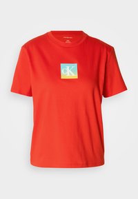 Rode katoenen t-shirt met ronde hals, voorzien van een vierkante grafiek met "cK" in wit en blauw, tegen een gradient achtergrond.
