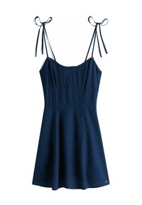 Vestido sin mangas azul marino con tirantes anudados, cintura ceñida, falda ligeramente acampanada y pequeños detalles de flores rojas cerca de los tirantes.