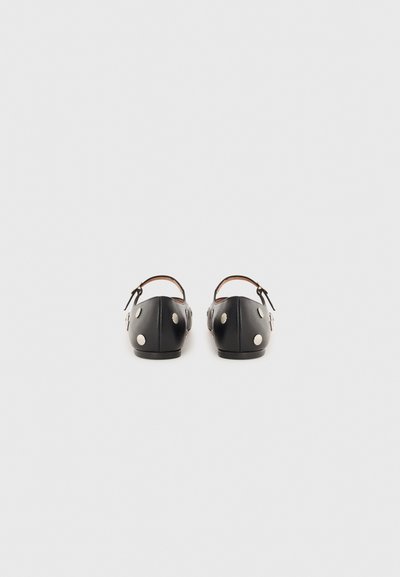 Black shoes with rounded backs, ankle strap, and metallic circular accents. Smooth texture with a flat sole and minimalistic design.