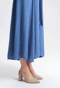 Blue, flowing maxi dress with a textured fabric, paired with beige suede slingback heels featuring a chunky heel and pointed toe.