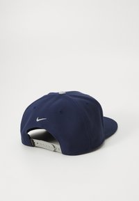 Marineblå kasket med en buet skygge, lavet af bomuld, med et broderet hvidt Nike-logo på bagsiden og et justerbart plastikspænde.