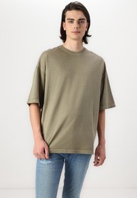 Olivengrøn oversized t-shirt i blødt stof, med korte ærmer og rund halsudskæring, parret med lyseblå slidte jeans.
