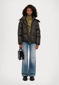 Giacca imbottita marrone scuro con finitura lucida; dolcevita a fantasia; jeans a gamba larga blu chiaro; borsa nera; scarpe con plateau.