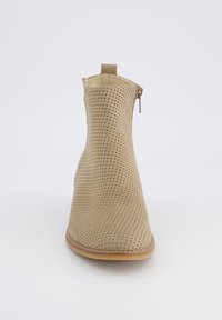 Botín beige con diseño perforado, textura suave, punta redondeada y detalle de cremallera lateral. Forro interior suave y suela flexible.