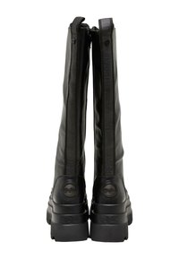 Botas negras hasta la rodilla con un acabado de cuero suave, con cremallera destacada y acento de logo texturizado en el tacón. Suela gruesa y forma estilizada.