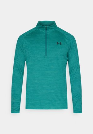 Türkiissinine pikade varrukatega poollukuga pluus tekstuurse kangaga, keskse luku ja musta Under Armouri logoga rinnal.