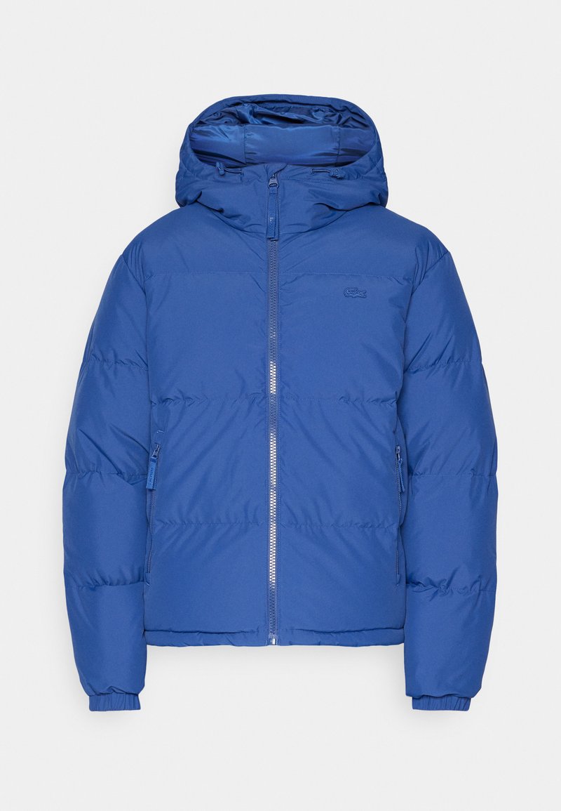Chaqueta acolchada azul con capucha, que presenta un cierre frontal, puños elásticos y un diseño acolchado. Logo pequeño en el pecho.