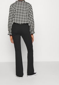 Černé rozšířené kalhoty a černobílá kostkovaná košile s dlouhým rukávem a volánkovými manžetami, doplněné o černobílé tenisky.