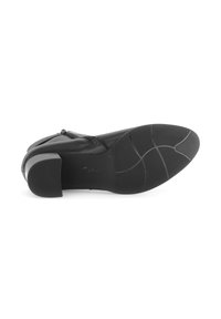 Bottine en cuir noir avec un petit talon carré, motifs de semelle visibles, et fermeture à glissière sur le côté, reposant sur le côté.