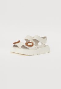 White platform sandals with two wide straps and a decorative brown bead detail. The sole is thick and textured for added grip.