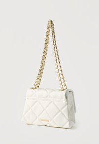 Λευκή τσάντα χειρός με καπιτονέ σχεδίαση, χρυσές αλυσίδες λουριά και μικρή χρυσή πλακέτα με λογότυπο σε απλό φωτεινό φόντο.