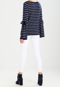 Námořnický a bílý pruhovaný top s dlouhými rukávy a rozšířenými rukávy uvázanými na manžetách, spárovaný s bílými skinny džíny a námořnickými kotníkovými botami.