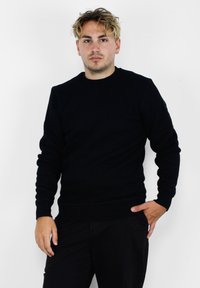 Felpa nera a girocollo realizzata in tessuto morbido, con polsini e fondo a costine, dal design minimalista e senza motivi o logo visibili.