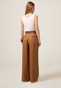 Pantalones de pierna ancha marrones con una textura suave, dos bolsillos traseros y un cinturón marrón, combinados con una blusa sin mangas blanca lisa.