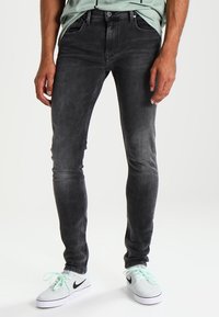 Černé džíny skinny z denimu s hladkým povrchem, obsahující pět kapes a vybledlý vzhled. Nosené s světle šedými teniskami a tričkem v mátové zelené barvě.