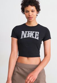 Črna skrajšana majica s kratkimi rokavi, z izrazitim sivim logotipom "NIKE" na sprednji strani. Gladek material, oprijet kroj.