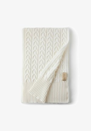 Kremowy, dziergany koc z haftowanym wzorem warkocza, żeberkowymi brzegami oraz małą tkaną metką. Miękka faktura o gęstym, ciepłym wyglądzie.