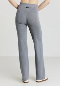 Pantalons en tricot gris avec une taille élastique haute, jambes droites et une texture douce ; portés avec des chaussures blanches à semelles marron.