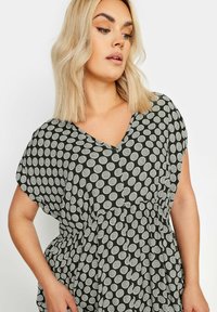 Svart klänning med vitt cirkulärt mönster, korta ärmar, V-enskärning, rynkad midja och lättviktig tyg som skapar en avslappnad siluett.