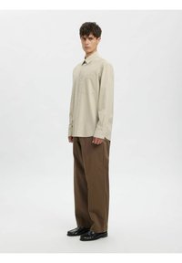 Beige rutete skjorte med lange ermer og knappelukking, kombinert med brune vide bukser og svarte sko, med en avslappet fasong og tekstur.