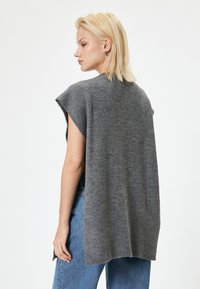 Top grigio senza maniche in maglia con una vestibilità comoda, caratterizzato da un collo alto, spalle cadenti e orlo posteriore leggermente più lungo.