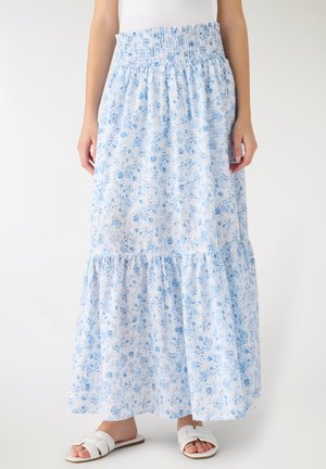 Gonna lunga bianca con stampa floreale blu, vita arricciata, orlo a balze, indossata con sandali bianchi e una maglia bianca.