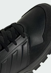 Primer plano de una zapatilla negra que muestra cuero texturizado, paneles de ante, cordones gruesos y una suela con un diseño robusto.