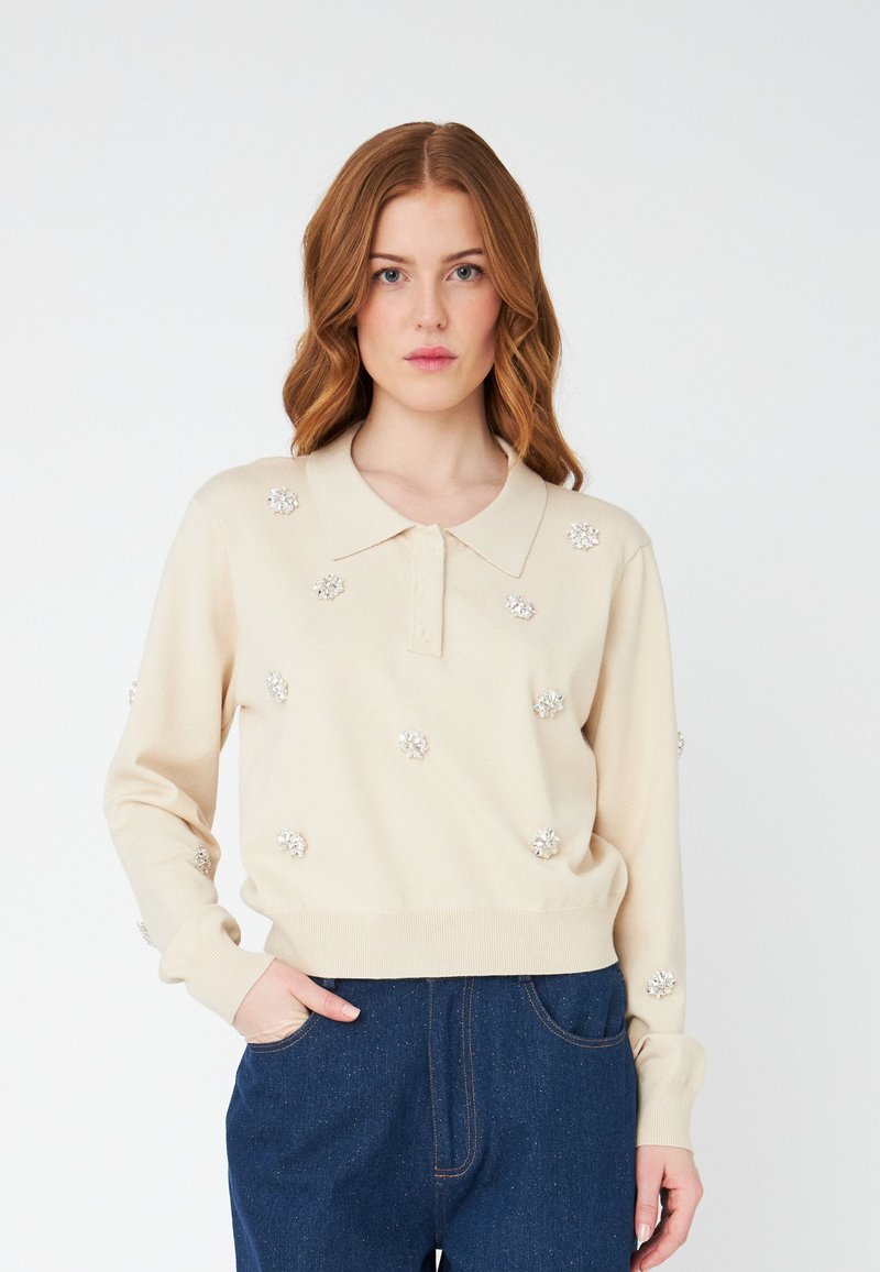 Maglione color crema con colletto polo, decorato con applicazioni floreali argento. Presenta maniche lunghe e polsini e orlo a coste.