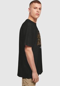 Sort bomulds T-shirt med korte ærmer, afslappet pasform, med farverigt grafisk design på forsiden i orange og hvid.