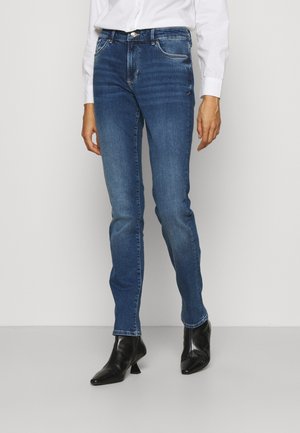 Jeans ajustados azules en un lavado desgastado, con cinco bolsillos, herrajes plateados y un leve desgaste. Combinados con botas de tobillo negras y de punta.