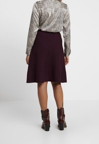 En knälång, utsvängd kjol i mörklila tyg, tillsammans med en mönstrad blus och blanka bruna ankelstövlar med en tjock klack.