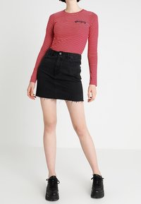 Röd- och vitrandig långärmad tröja med en figurnära design, ihop med en svart denim minikjol med fransad nederkant och svarta platåskor.