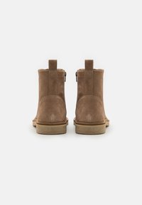 Botas de tobillo de ante marrón con una textura suave, puntera redondeada y una suela de goma baja. Cremalleras laterales y tiradores para ponerlas y quitarlas fácilmente.