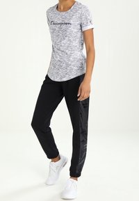 Gray short-sleeve T-shirt with "Champion" logo and black sweatpants featuring a textured side panel. White athletic shoes.