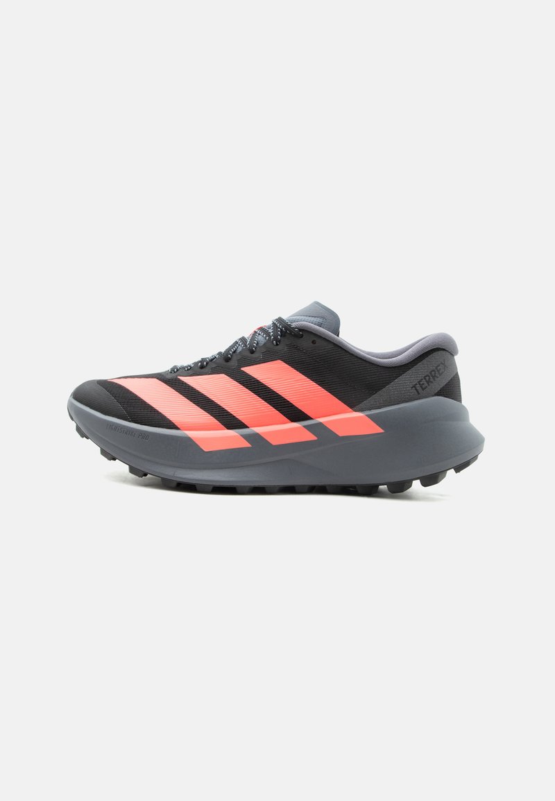 Chaussure de sport noire et grise avec des bandes orange vif, semelle épaisse et fermeture à lacets, conçue pour une utilisation extérieure ou sur sentier.