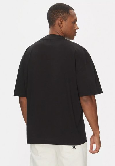 T-shirt nera oversize con maniche corte, scollatura rotonda e design semplice. Presenta un sottile dettaglio del logo sulla parte bassa della schiena.