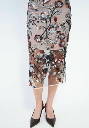 Gonna trasparente con motivi floreali ricamati in colori metallici e pastello, indossata con décolleté nere con punta appuntita.