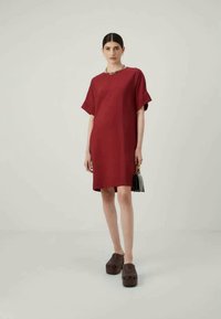 Κόκκινο, φαρδύ φόρεμα κοντό μανίκι με ίσια γραμμή, ύψους γόνατου, συνδυασμένο με σκούρες μπότες και μια μικρή μαύρη τσάντα.