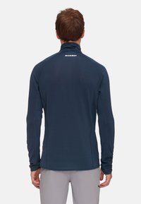 Maglietta a maniche lunghe blu marina con colletto alto, dotata di cuciture piatte e un piccolo logo sul retro. Texture liscia con design aderente.