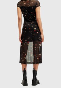 Musta läpinäkyvä mekko, jossa on kukkakuosi, lyhyet hihat ja keskipitkä leikkaus. Yhdistetty mustiin nilkkasaappaisiin.