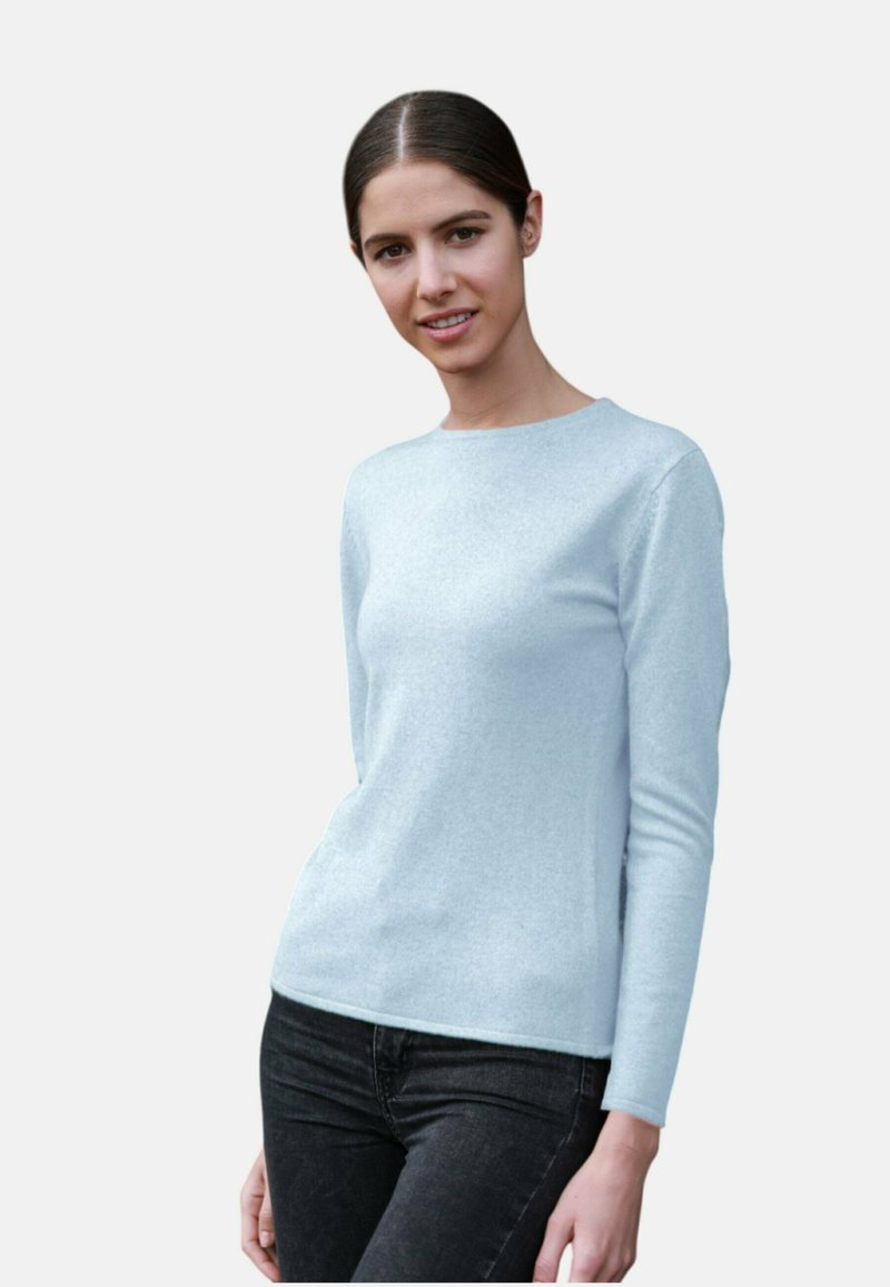 Pull long bleu clair en tissu doux, avec un col rond et une silhouette ajustée, associé à un jean foncé.