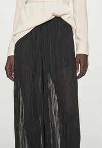 Black pleated wide-leg pants with a textured sheer material, featuring a high-waisted design and a loose fit for added comfort.