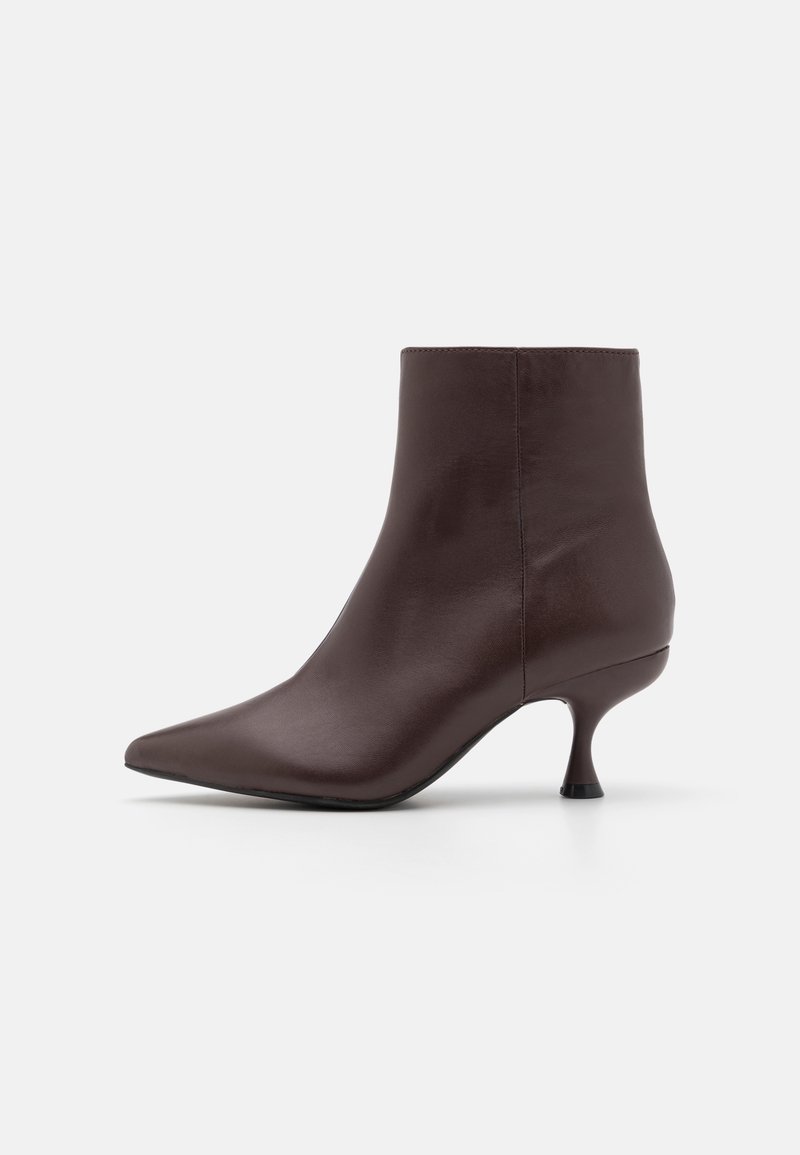 Bottine en cuir marron foncé avec bout pointu et talon aiguille fin, sur un fond clair uni.
